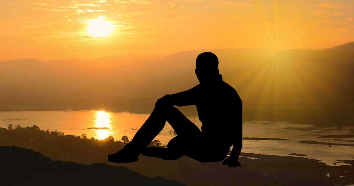 Silhouette of a person meditating at sunset over a river