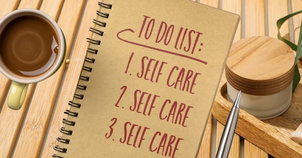 Notebook showing a to-do list with "Self Care" written three times, next to a cup of coffee and skincare items on a wooden surface.