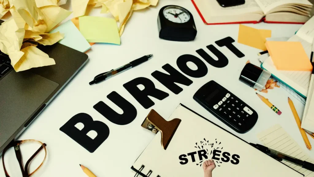 Desk cluttered with papers, calculator, clock, and the word burnout—symbolizing stress and why you can’t focus