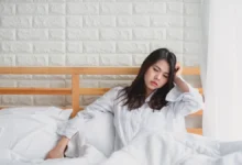 Tired woman sitting on bed feeling emotionally exhausted in the morning.