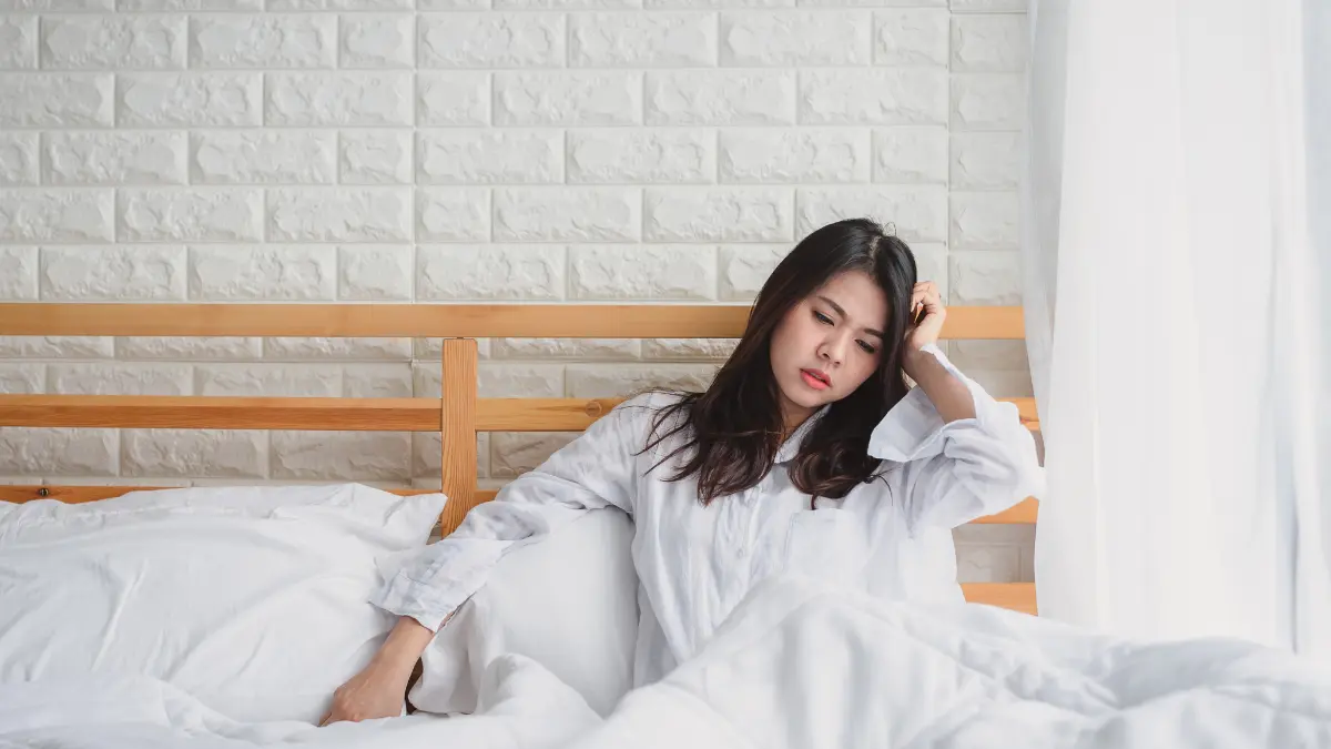 Tired woman sitting on bed feeling emotionally exhausted in the morning.